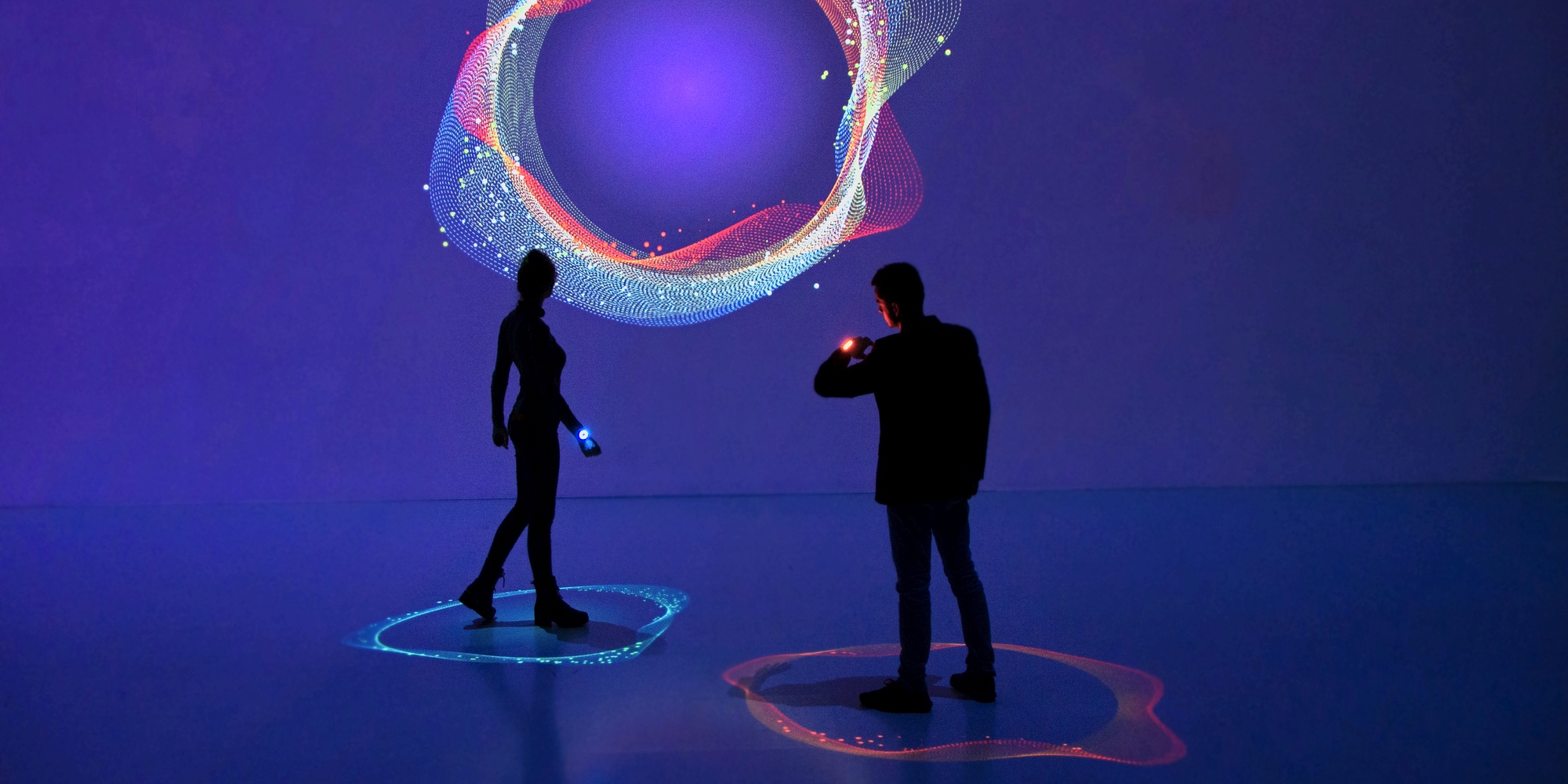 Two people in Deep Space with flashing devices on wrist displaying their heart beat on wall projection