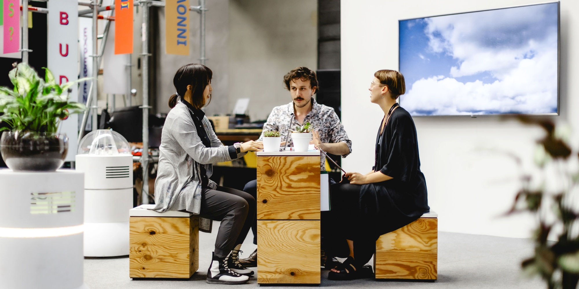 3 team members seated around small table surrounded by robots ("future buddies")